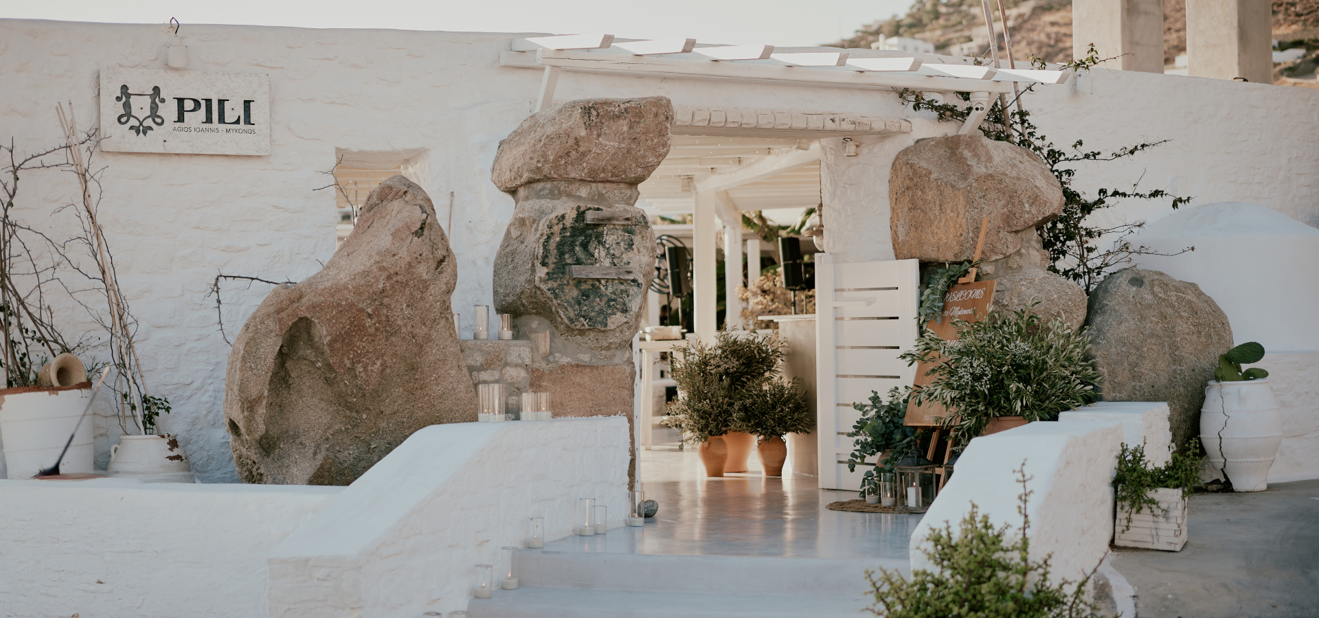 The venue entrance of the Greek themed pre wedding event, depicting a white wall with rocks and Olive tree inspired décor.