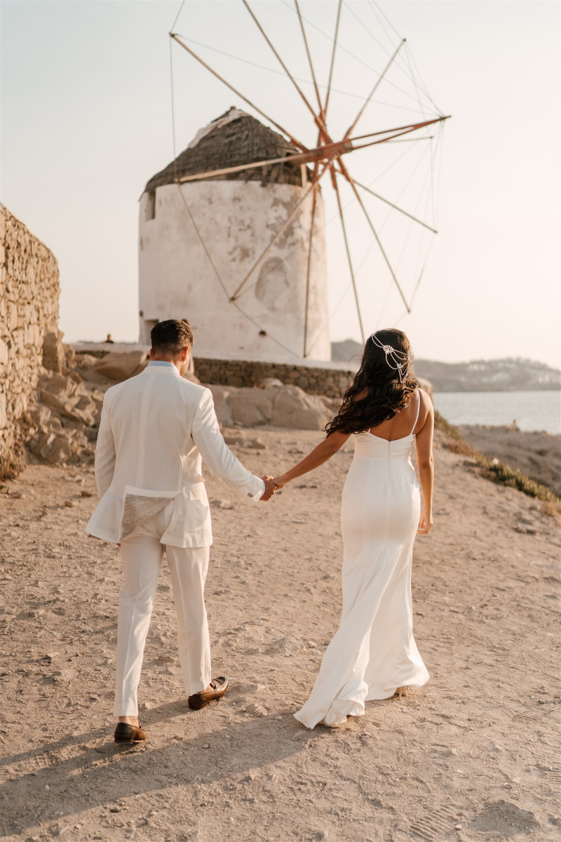 A newlywed couple holding hands at a dreamy wedding in Mykonos with windmills as the backdrop.